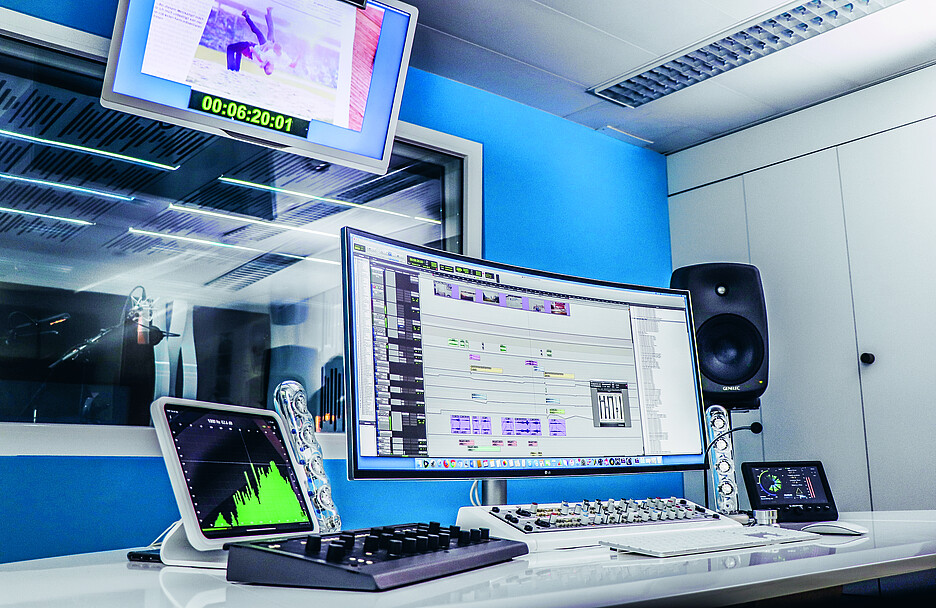 <em>Salle de régie des studios d’enregistrement Bluebox à Berthoud. Au fond à gauche de l’image, la cabine du speaker avec le microphone.</em>
